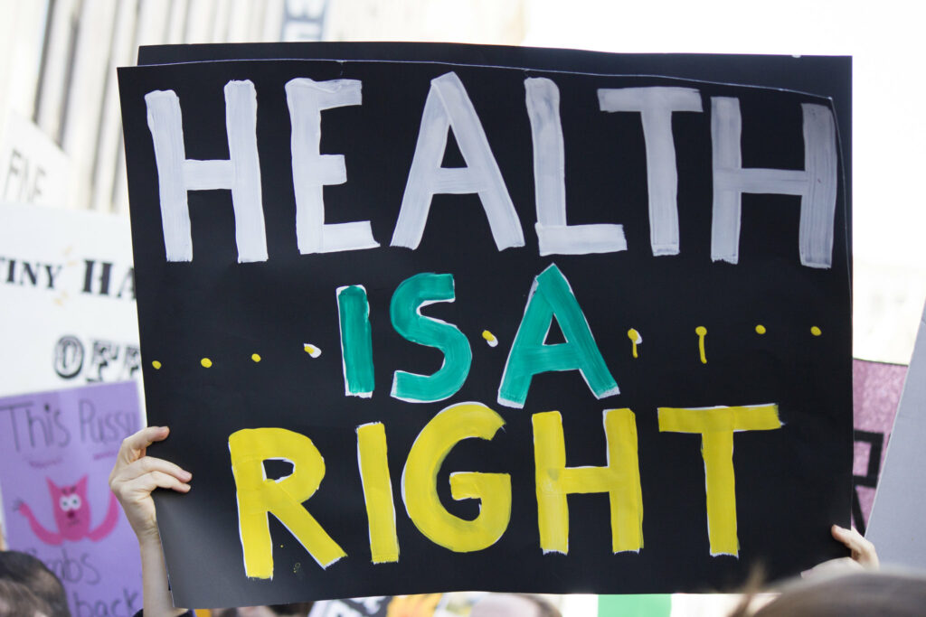 Schild auf einer Demo, das hochgehoben wird und auf dem der Text "Health is a right" in Blockbuchstaben geschrieben ist
