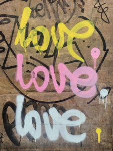 auf einer Hauswand steht dreimal das Wort "love" in jeweils unterschiedlichen Farben - gelb, rosa und hellgrau