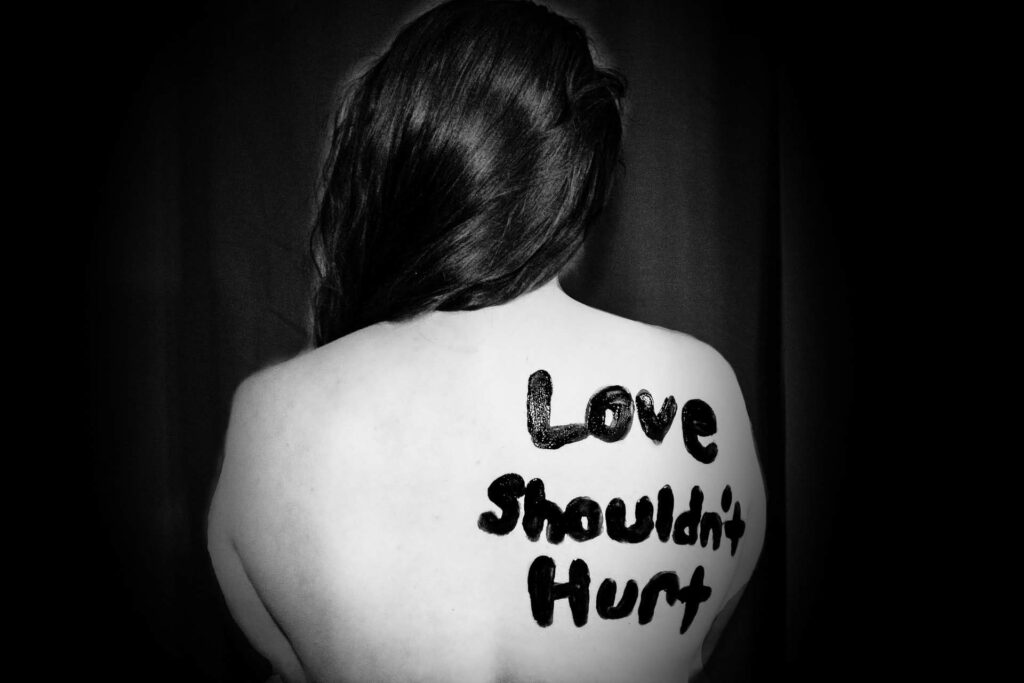 schwarz-weiß Bild vom Rücken einer Person, auf dem in schwarzer Farbe der Text "Love shouldn't hurt" geschrieben ist