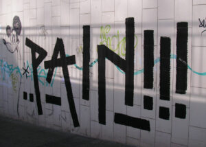 Mauer mit Graffiti und Tags, im Vordergrund steht der Text "PAIN!!!".