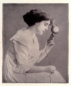 Frühe Vibrator-Werbung: eine junge Frau in weißem Rüschenkleid hält einen Vibrator an ihre Stirn
