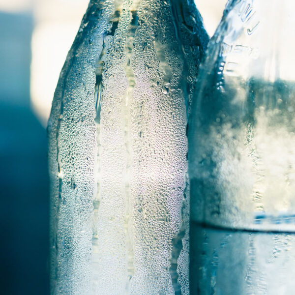 Zwei schwitzende Glasflaschen, das Bild ist in blau-weiß Tönen