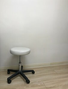 Rollhocker mit weißem Sitz vor einer weißen Wand