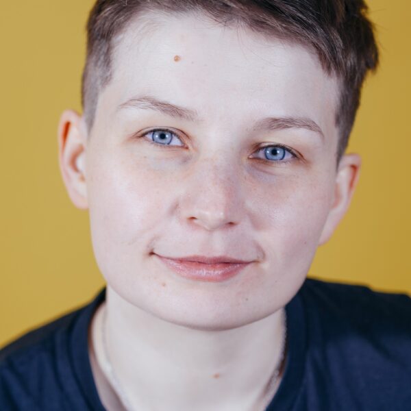 Porträtfoto von Sara Grzybek. Sara hat kurze braune Haare, trägt ein dunkelblaues Oberteil und lächelt in die Kamera