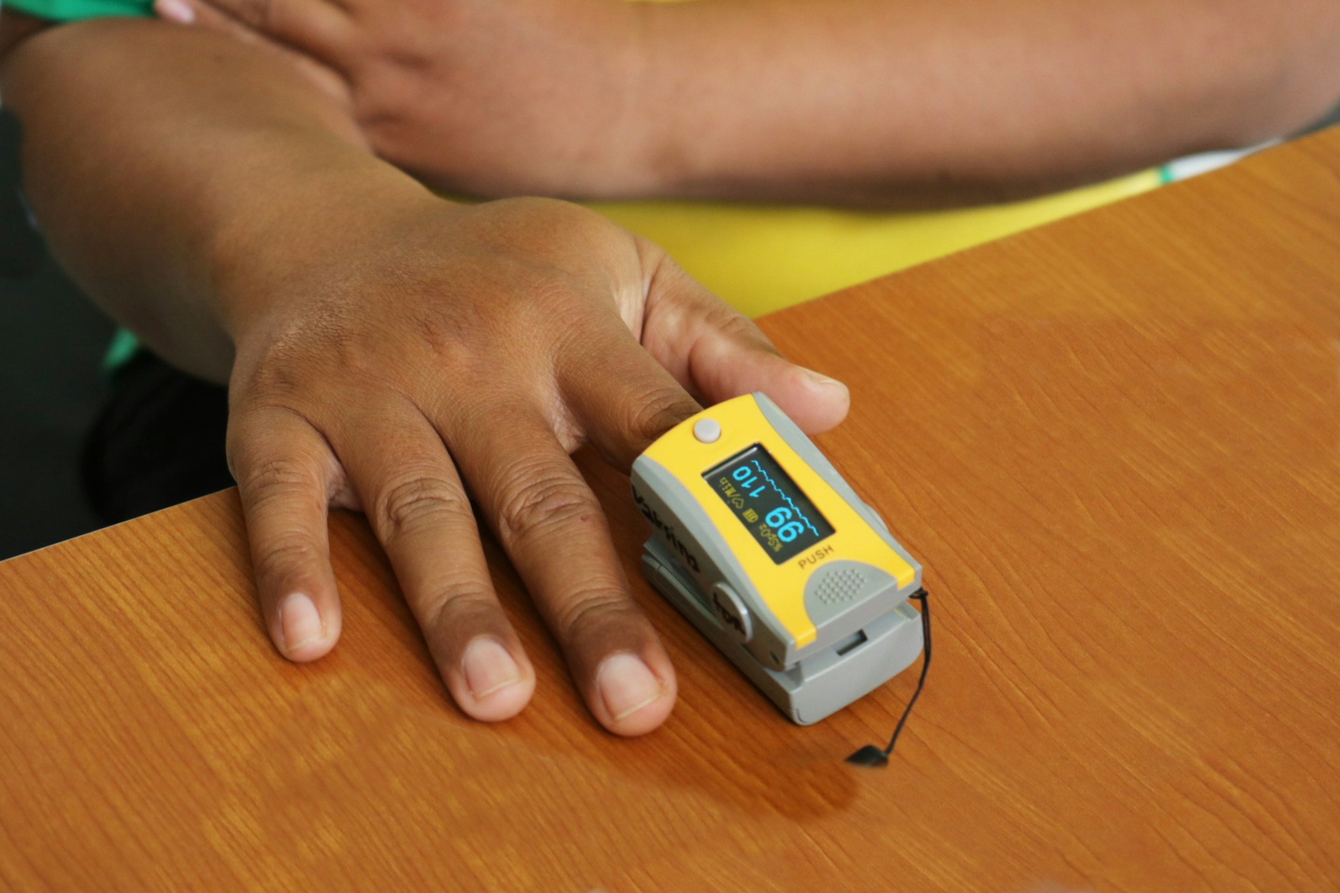 Eine Hand mit dunkler Hautfarbe liegt auf einem Tisch, ein Pulsoxymeter misst an einem Finger den Sauerstoffgehalt.