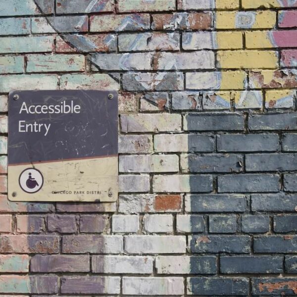 Mauer aus Ziegelsteinen mit Graffiti und einem Schild mit dem Text "Accessible Entry" und einem Piktogramm von einer Person im Rollstuhl
